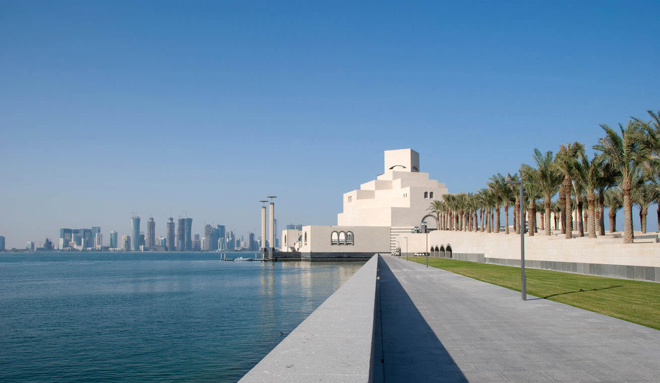 A wide-angle image of the Museum of Islamic Art, one of the main architectural and cultural landmarks in Doha, Qatar, set against the backdrop of the city skyline.